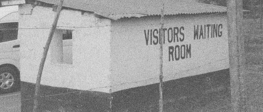 A hut with corrugated metal roof, with the words 'Visitor waiting room' painted on its wall